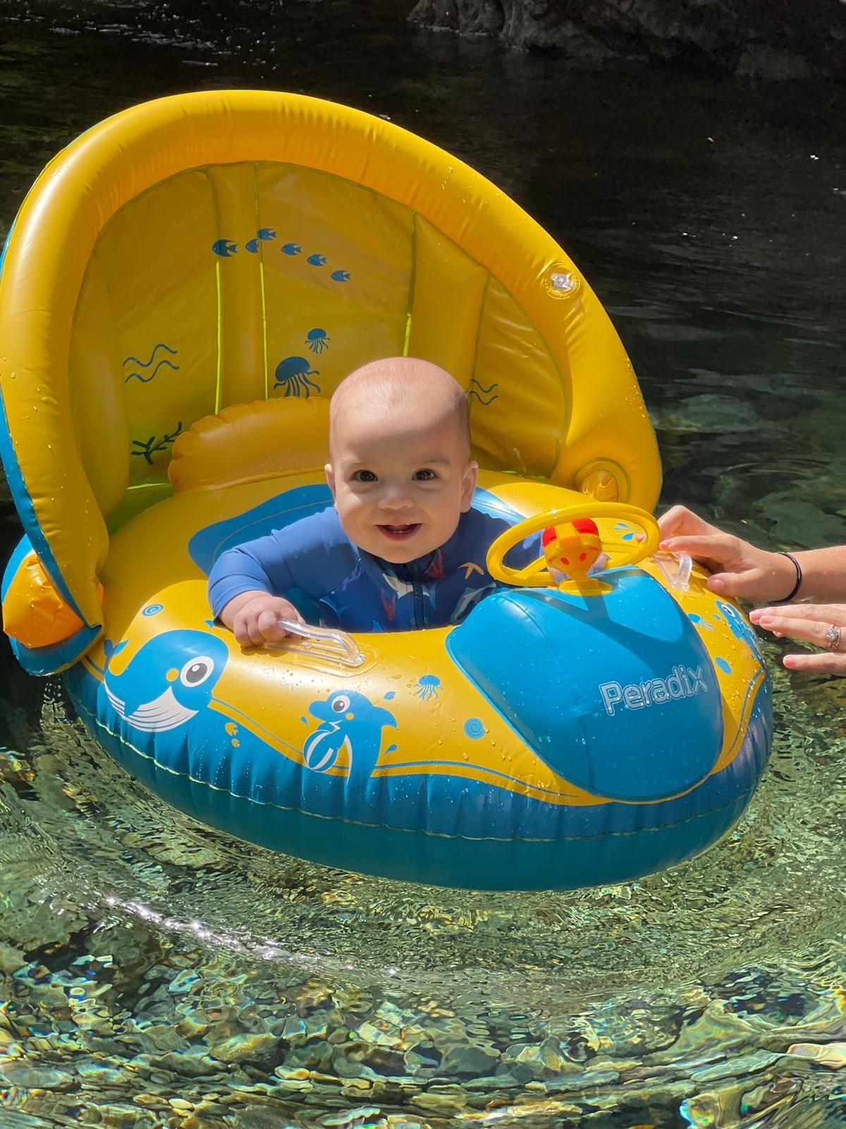 Baby smiling in a yellow and blue baby boat float in clear water