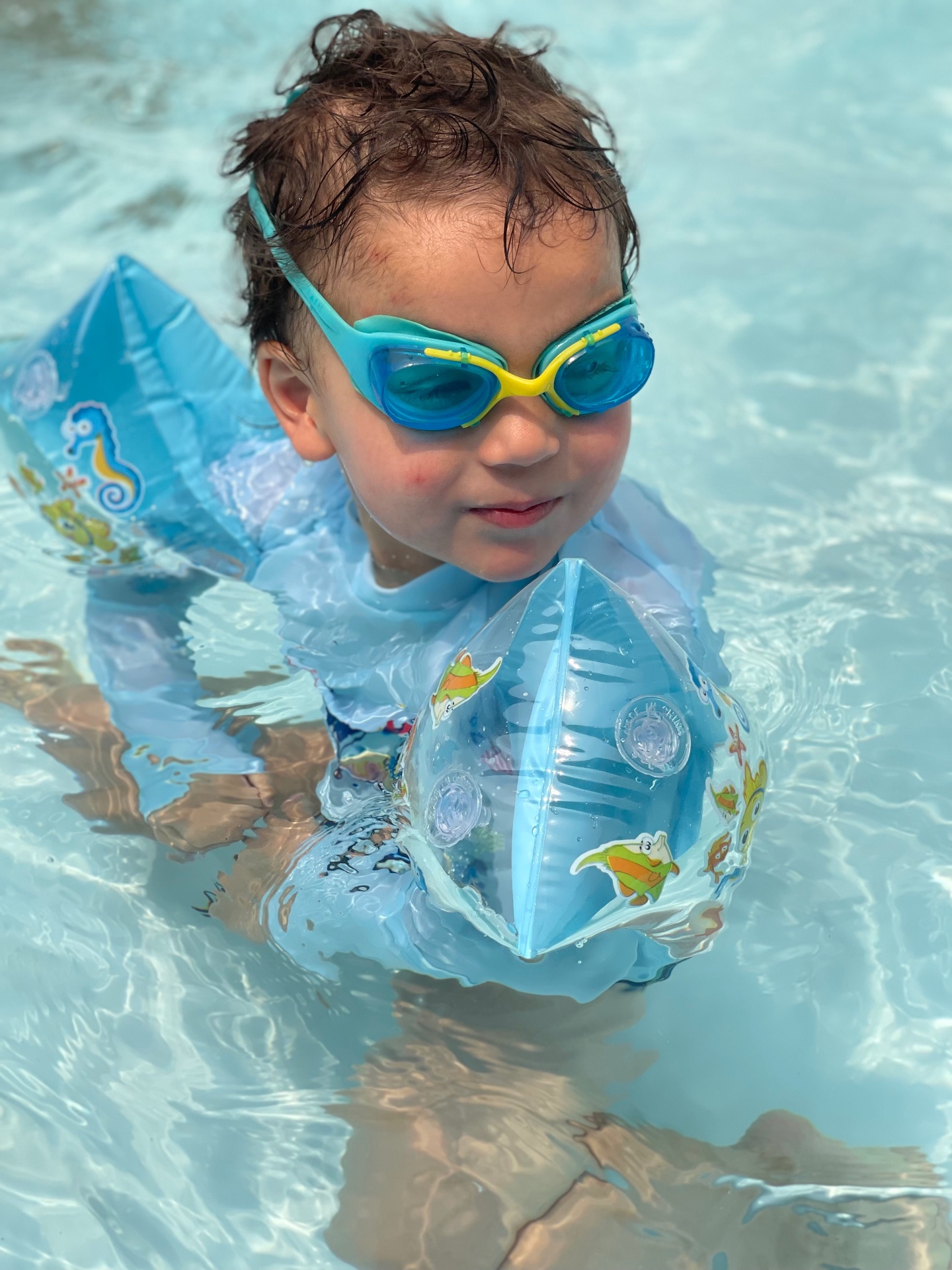 Toddler with goggles and floaties swimming in a clear pool