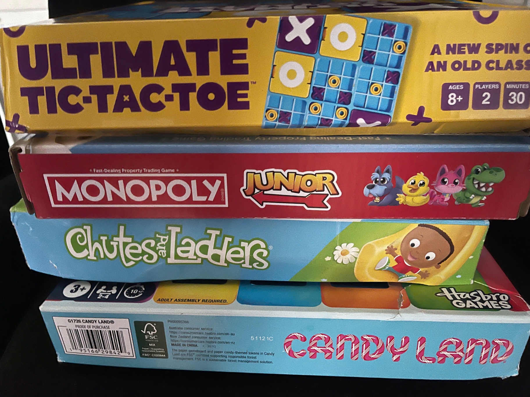 A stack of family board games including Ultimate Tic-Tac-Toe, Monopoly Junior, Chutes and Ladders, and Candy Land
